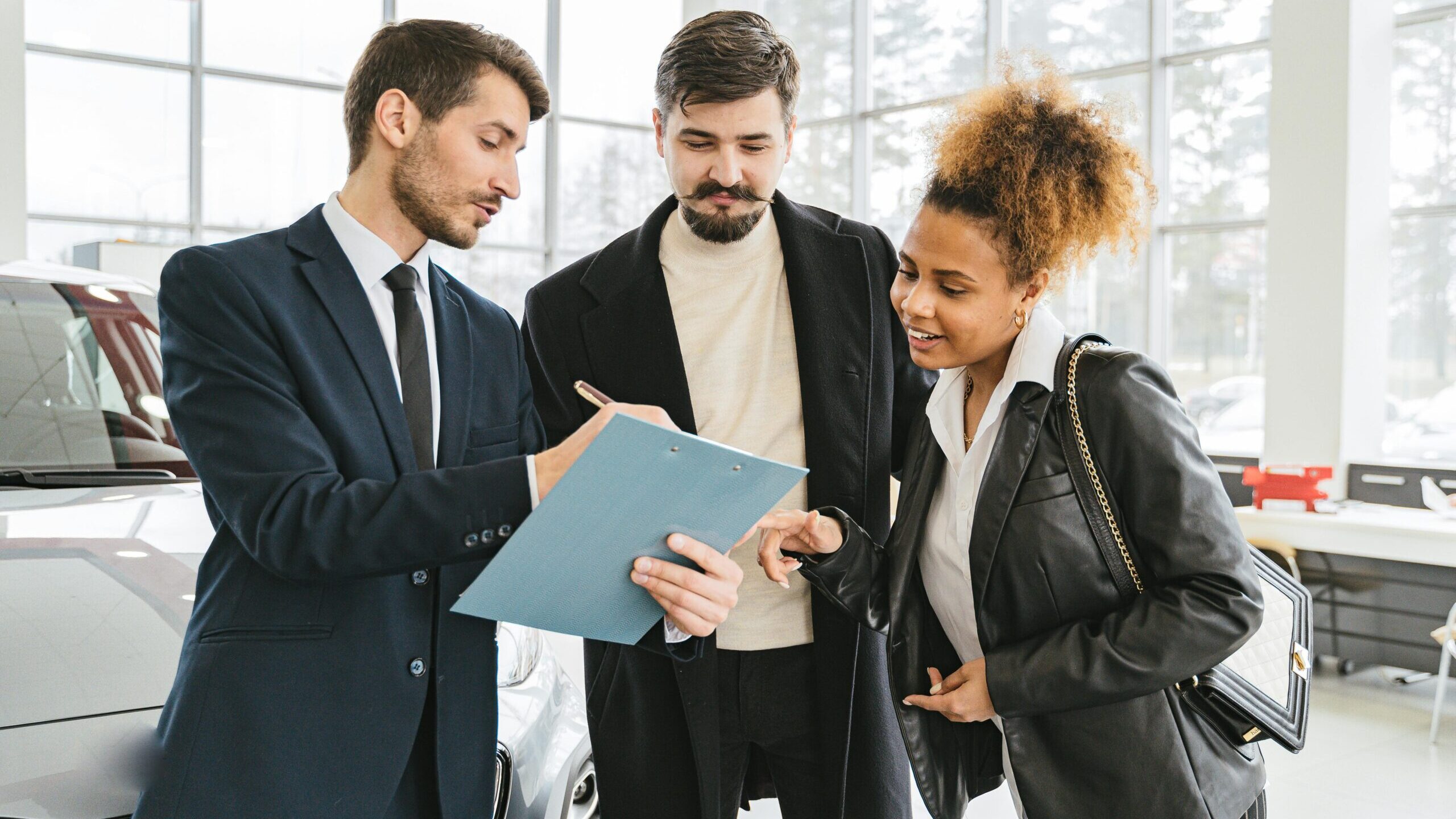 Three business professionals discussing car purchase details inside a modern dealership.
