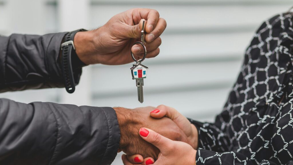 Close-up of a realtor handing over a house key to a new homeowner, symbolizing ownership and investment.